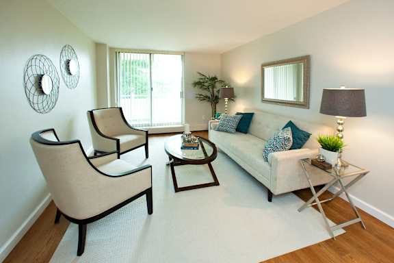 A living room with a white couch, two chairs, and a small table with a lamp on it.