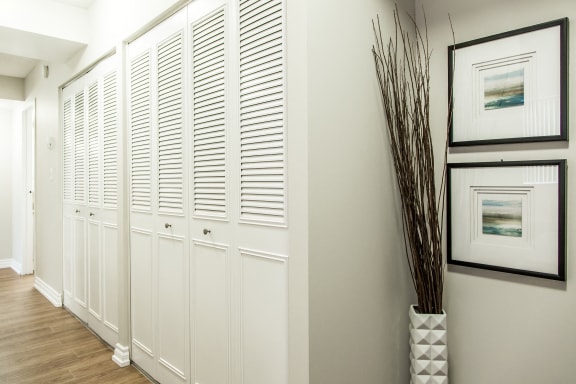 a hallway with white shutters on the wall and a vase on the floor