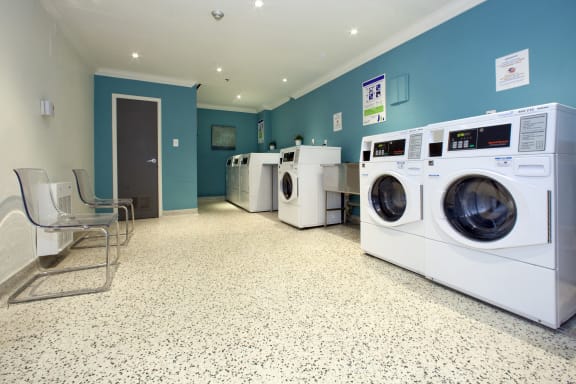 a washer and dryer room with four washing machines and chairs in a laund