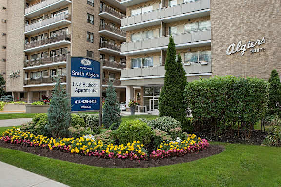 an apartment building with a sign in front of a flower garden