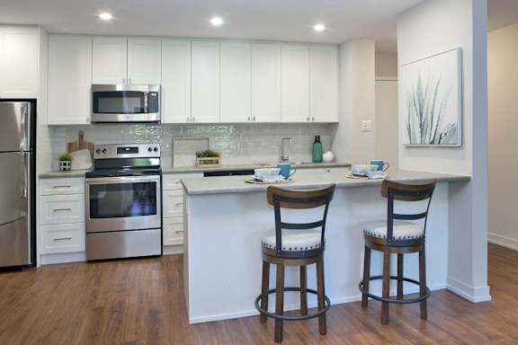 a kitchen with white cabinets and a counter with two chairs