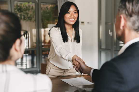 A woman shakes hands with a man at a table.