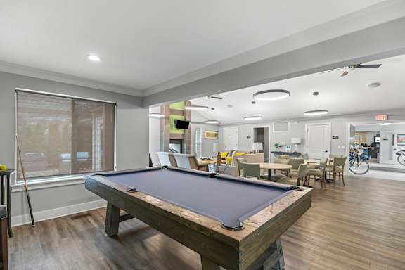 A pool table is in the middle of a room with a bicycle in the background.