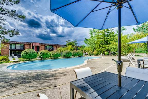A blue umbrella is over a table in front of a pool.