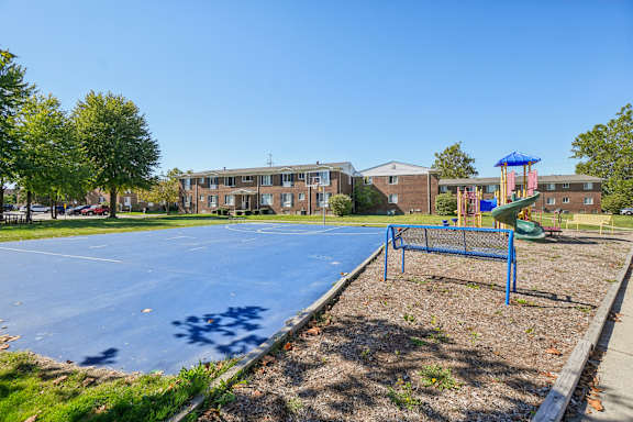 A basketball court in a park with a playground in the background.