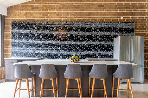 A kitchen with a brick wall and a bar area with grey chairs.