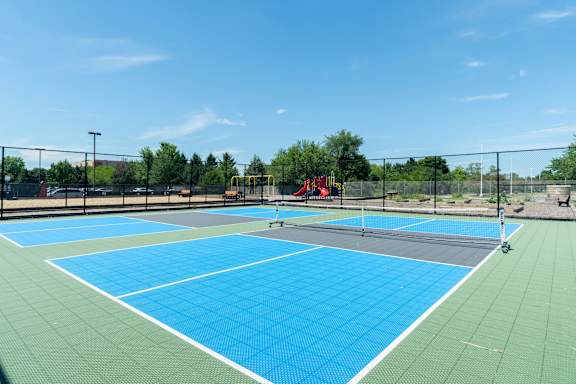 A tennis court with a blue surface and green surroundings.