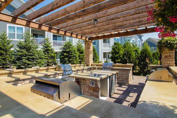 A patio with a grill and a table under a wooden pergola.