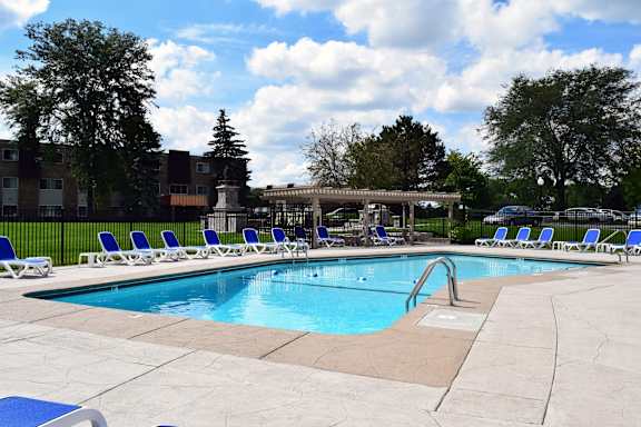 A swimming pool surrounded by chairs and trees.