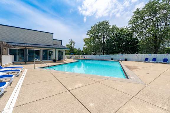 A large outdoor swimming pool with lounge chairs and a building in the background.