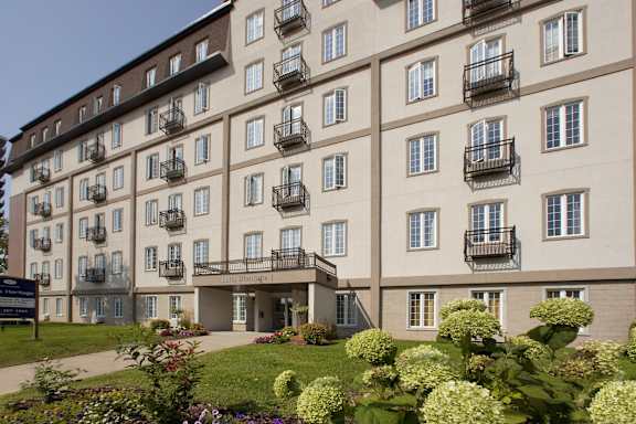 A large building with balconies and windows is surrounded by greenery.