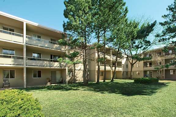 Apartment complex with green grass and trees in the foreground.