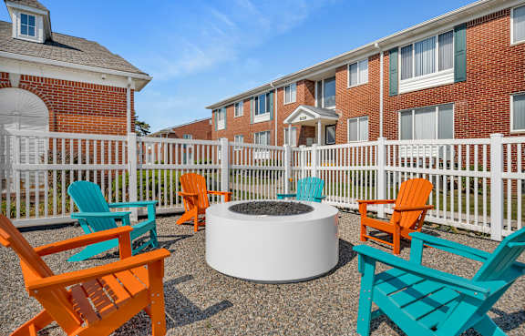 A white fire pit sits in the middle of a patio surrounded by colorful chairs.