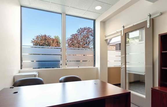 A conference room with a table, chairs, and a view of trees and buildings outside the window.