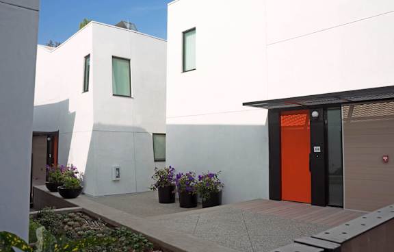 A modern white house with a red door and a black metal fence.