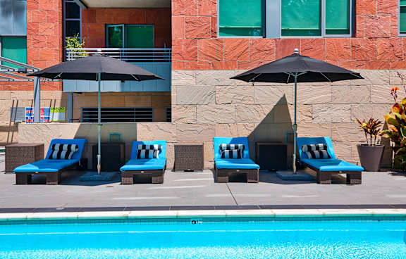 A pool with two lounge chairs and umbrellas in front of a building.at Catania, California, 91105