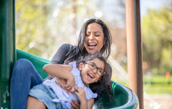 a woman sliding down a green slide holding a child