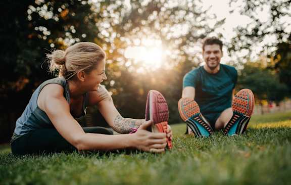 A man and a woman are sitting on the grass, stretching their legs.