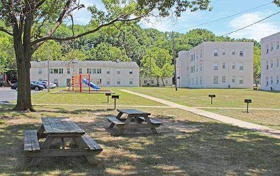 A playground with a slide and picnic tables in the foreground with buildings in the background.