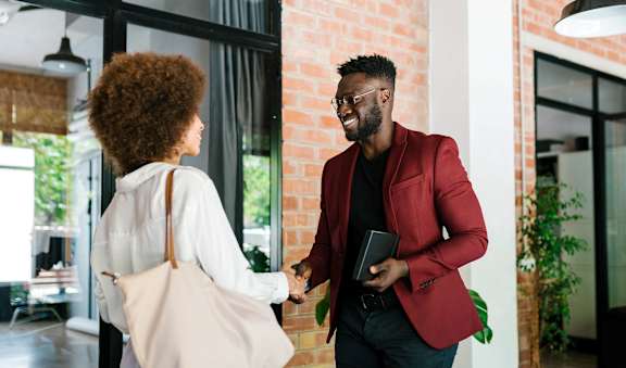 A man in a red blazer is shaking hands with a woman in a white blouse.