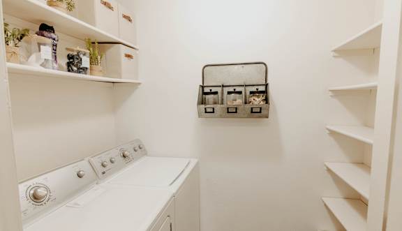 A white laundry room with a washer and dryer and shelves with storage containers.