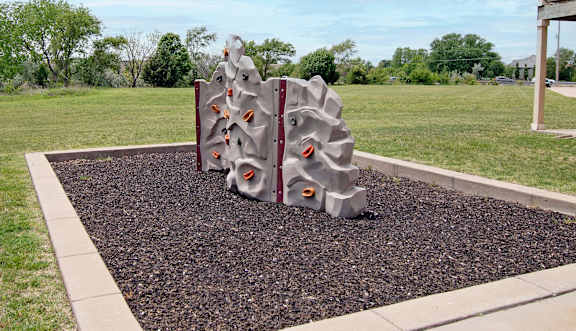 A playground structure with a grey and red color scheme is situated in a gravel area with a grassy background.