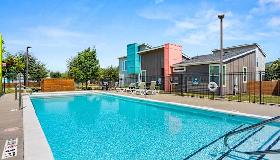 A large swimming pool with lounge chairs and a building in the background.