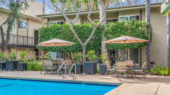 A pool surrounded by chairs and umbrellas in front of a building.