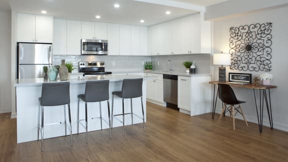a kitchen with white cabinets and a bar with three chairs