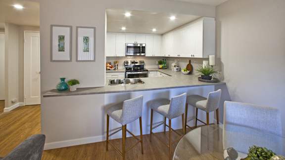 an open kitchen with white cabinets and a bar with three chairs