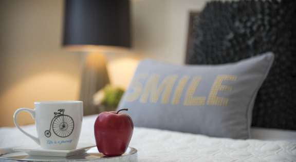 A cup of coffee with a bicycle design and an apple on a bed tray.