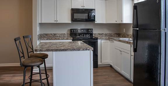 A room with a black fridge and wooden flooring.