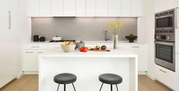 a kitchen with white cabinets and a white island with black stools