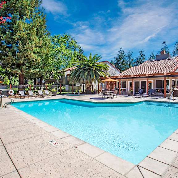 A large swimming pool surrounded by trees and a house in the background.