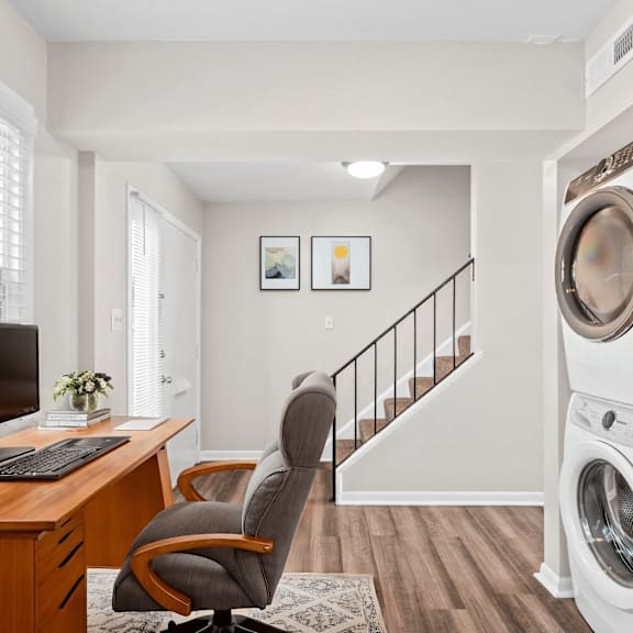 A washing machine is placed in a room with a desk and a chair.