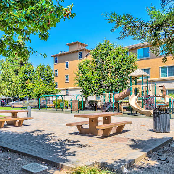 a park with a playground and picnic tables in front of a building