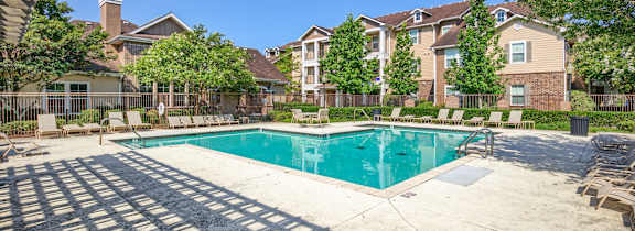A swimming pool surrounded by a concrete patio and residential buildings.