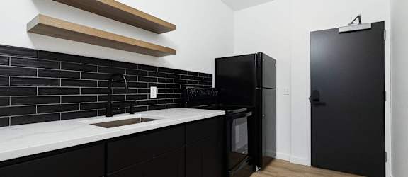 A modern kitchen with wooden shelves and black countertops.
