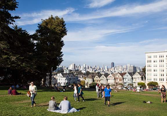 A group of people are sitting and standing on a grassy hill in a park.at The Rise, San Francisco, 94103