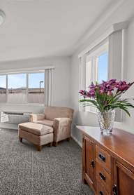 A living room with a purple couch, a chair, a small table, and a vase of flowers.