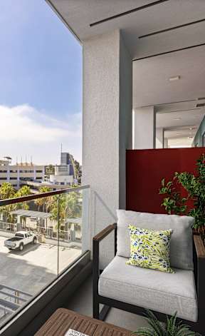 A balcony with a chair and a potted plant overlooks a parking lot and buildings.