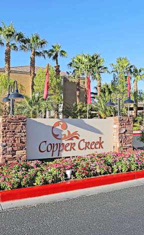 A sign for Copper Creek is in front of some palm trees.