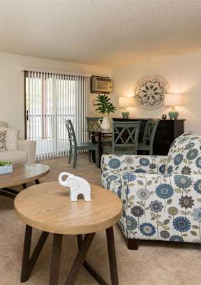A living room with a clock on the wall and a couch with a pillow on it at Rosemont Place Apartments, Des Moines, IA, 50320