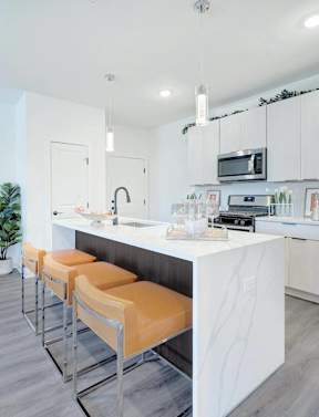 a kitchen with stainless steel appliances and a bar with orange stools at The Franklin at Hillsborough Apartments, NJ,08844