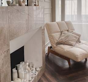 A white vase with a green plant sits on a white shelf next to a white curtain.
