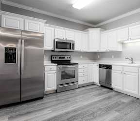 A kitchen with white cabinets and a bar area with stools.at Diamond Brooke, West Des Moines