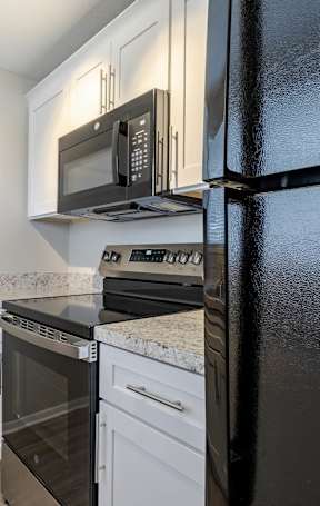 A black refrigerator stands next to a white oven and microwave in a kitchen. at Imperial Gardens Apartments, Clearwater, FL, 33764
