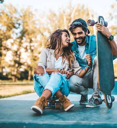 A man and a woman are sitting on a skateboard ramp, with the man holding the woman's hand.