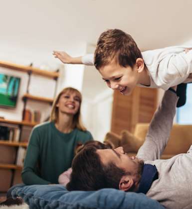 A man is lifting a child in the air while a woman watches.