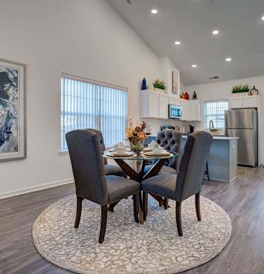 A dining room with a table set for two and a plant on the side table.